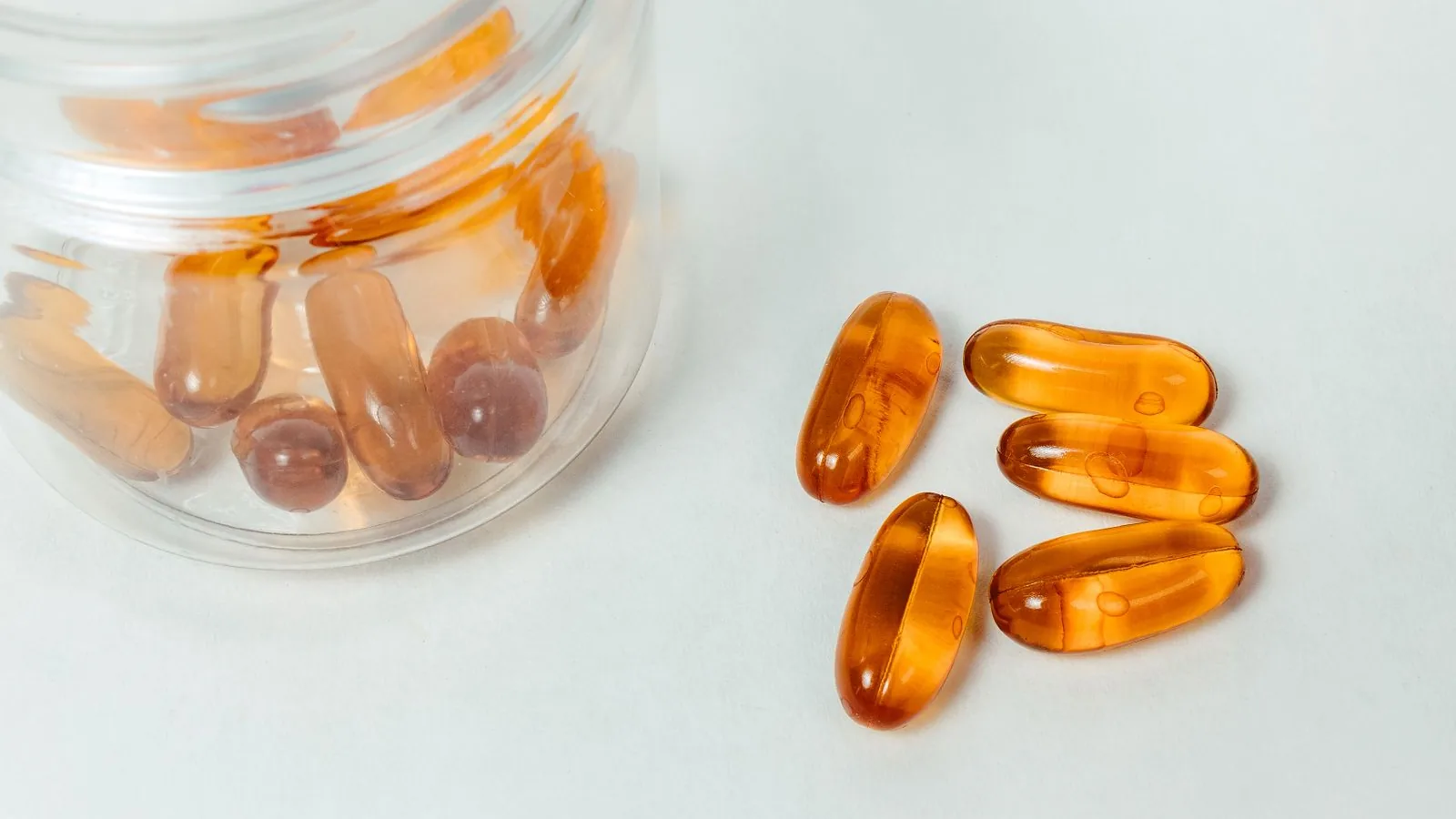 Amber softgel capsules spilling out of a glass jar onto a white surface