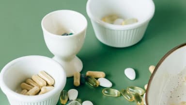 Capsules and softgels spilling out of small bowls on a green background