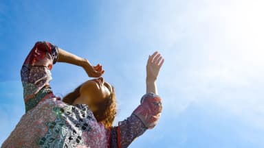 A person raising their arms toward bright sunlight against a clear blue sky