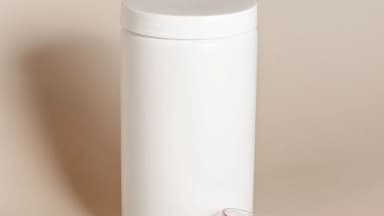 A white protein powder container with its scoop resting beside it