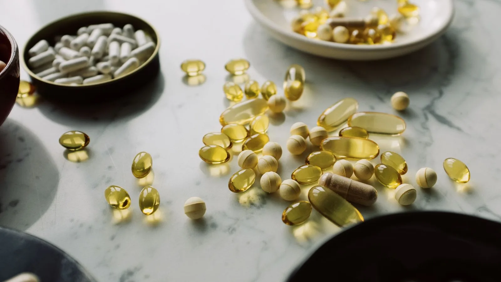 Assorted capsules and softgel supplements scattered across a marble surface